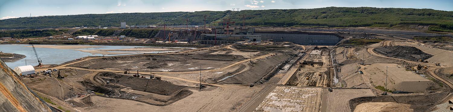 The earthfill dam continues to take shape, with the generating station and spillways under construction in the background. | August 2021