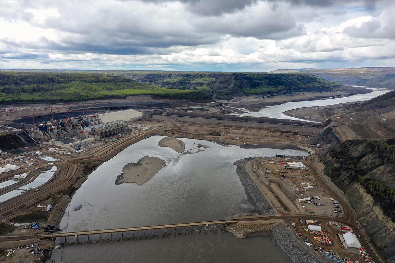 An upstream view of the powerhouse and generating station, with laydown areas, temporary fishway and outlet portals. | May 2022