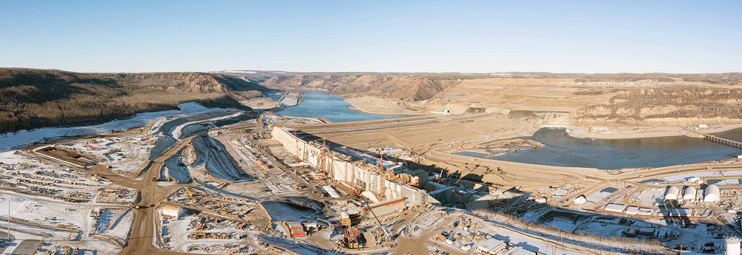 An upstream view with the approach channel at left, the powerhouse and generating station at centre, and the earthfill dam at centre. | November 2022