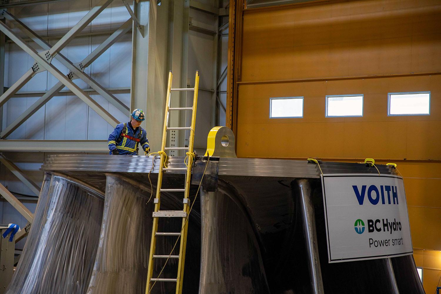 Workers connect a crane to lift the second turbine runner. There will be six turbine runners, each weighing about 165,000 kilograms. | March 2023