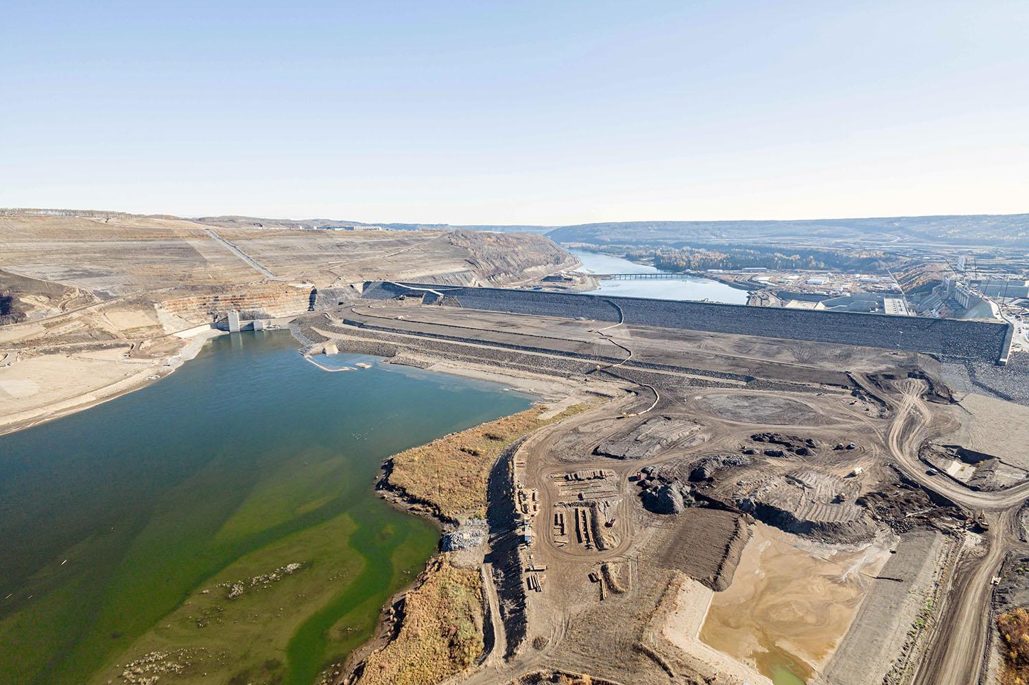 The earthfill dam stretches over one kilometre across the Peace River, which is currently flowing through the diversion tunnels to the left.