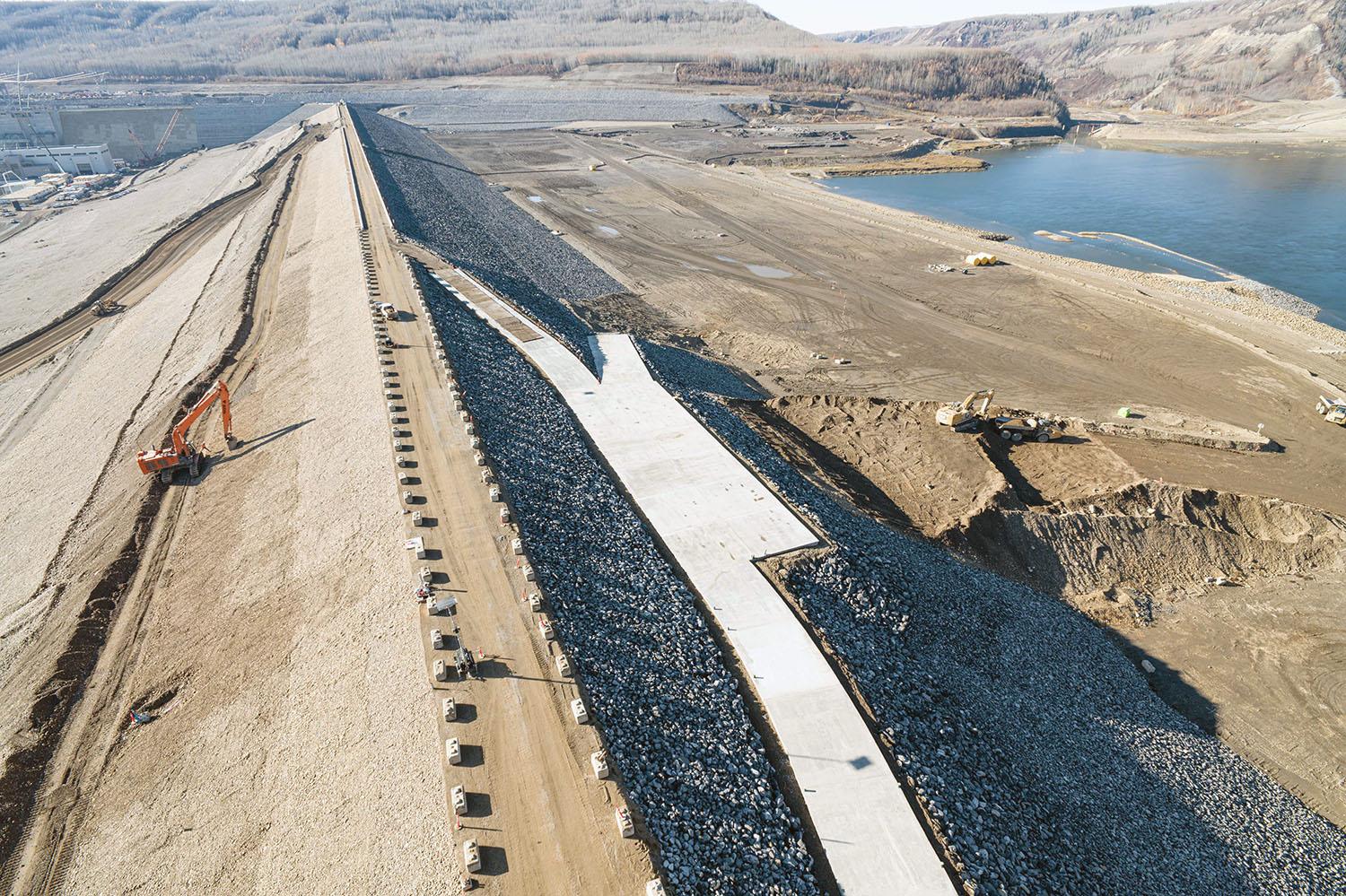 The top of the earthfill dam will be capped with asphalt. The ramp to the right is for debris management. There is an access road on the downstream side.