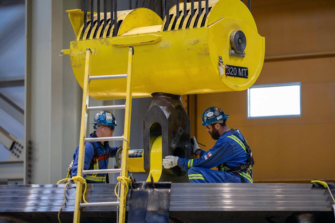 A crane is connected to a lifting device to install the second turbine runner. The runner is the heaviest single project component. | March 2023