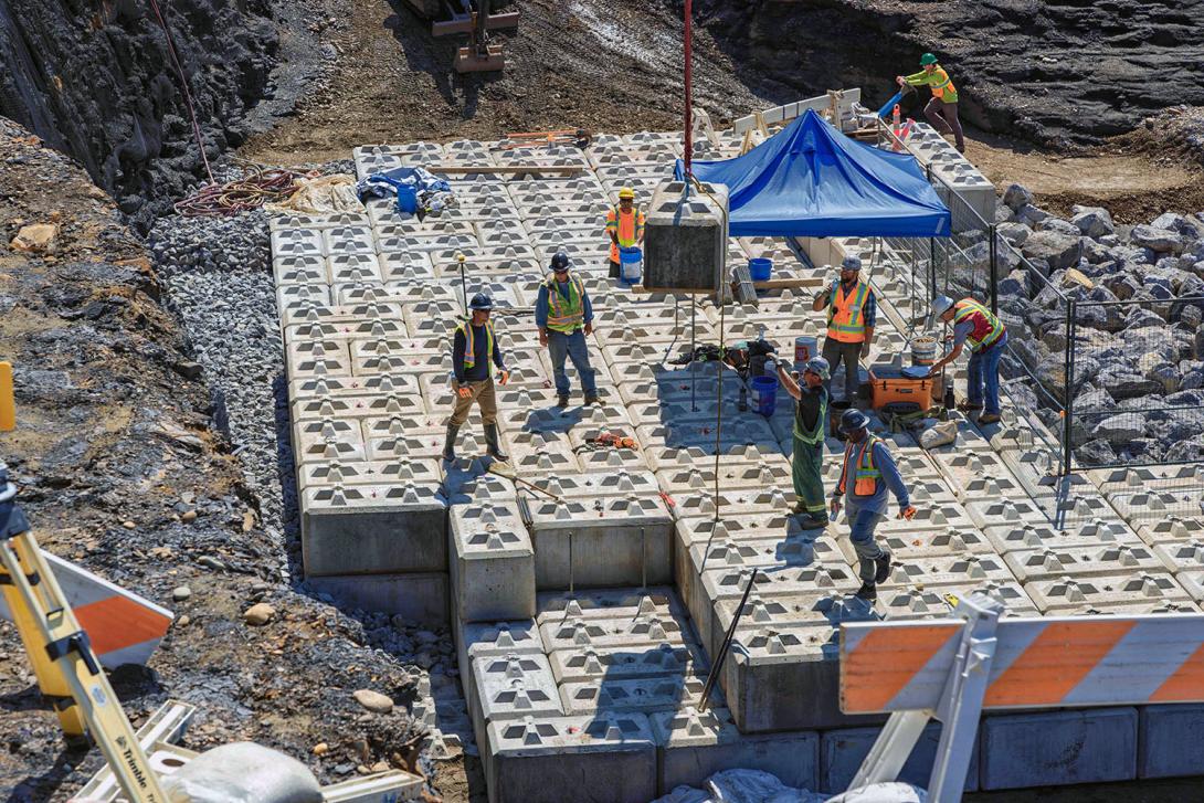 Concrete lock-blocks are carefully placed to construct the left bank drainage wall. Each concrete block weighs 2,000 kg. | July 2024