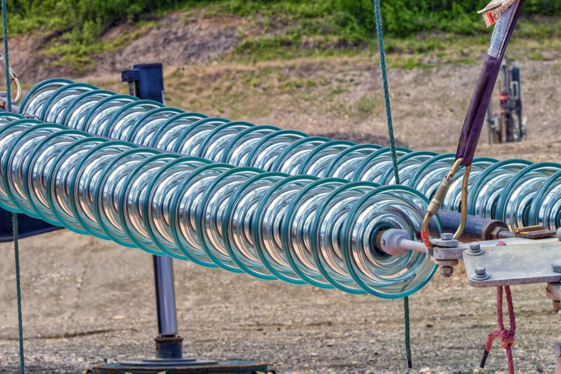 500-kilovolt dead-end glass is rigged ahead of raising into position. A spreader bar in the centre keeps the glass rigid. | June 2024