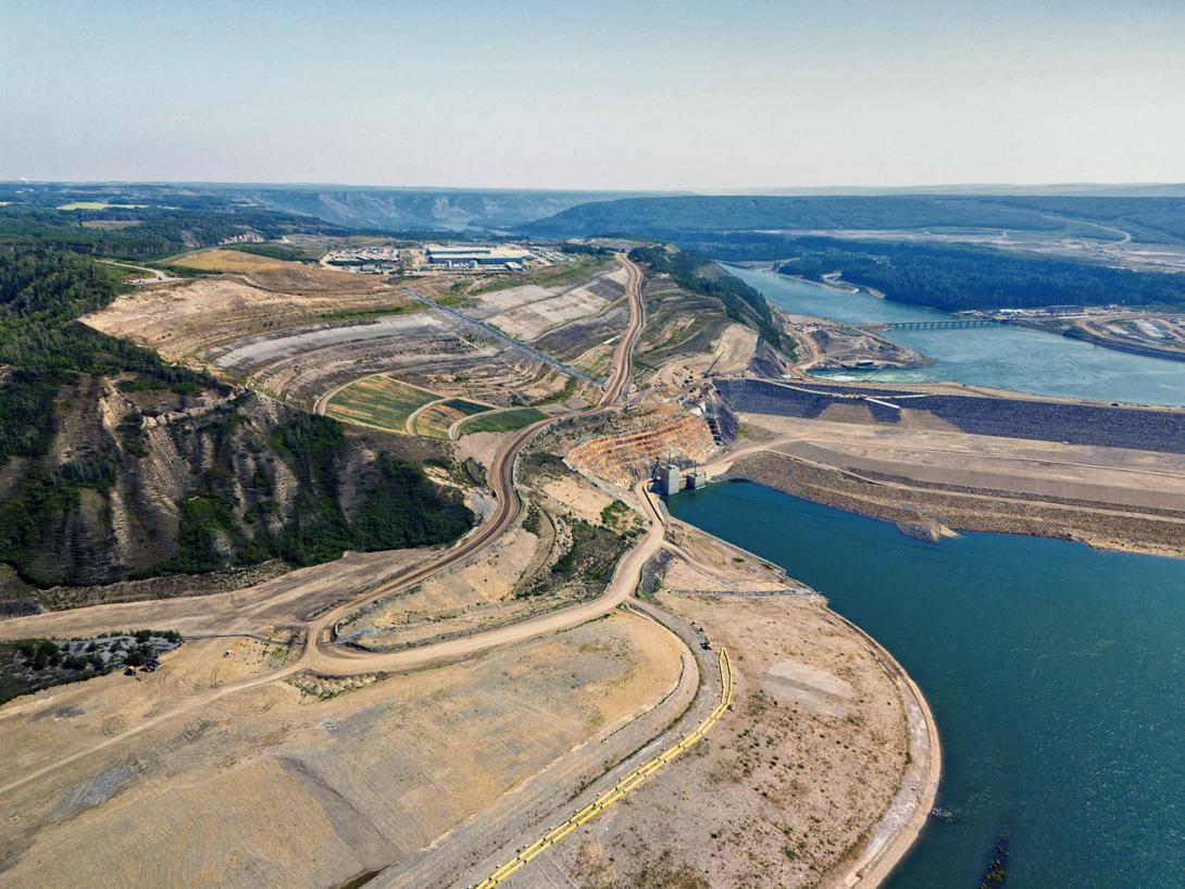 The reservoir area has been cleared. Slopes above the dam are scaled back and seeded, with the drainage management completed. The Peace River flows around the dam through the diversion inlet portal at centre. | August 2024