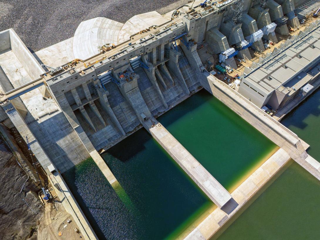 The spillway structure has a passive spillway (at left), three upper-level outlet gates, and six lower-level outlet gates. In the early stages of reservoir filling, water will flow through four of the lower-level outlet gates. | August 2024