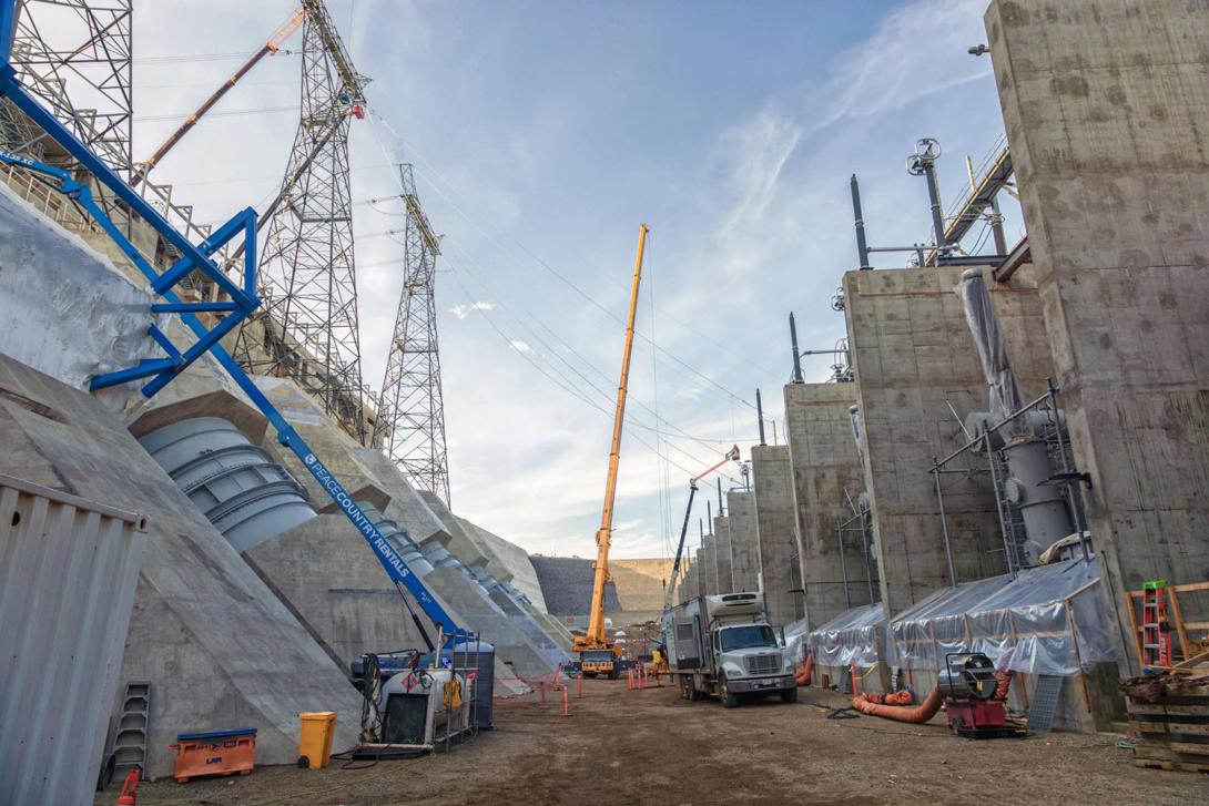 In the transformer yard, powerline technicians are connecting the line between the second transmission tower and the transformer. 